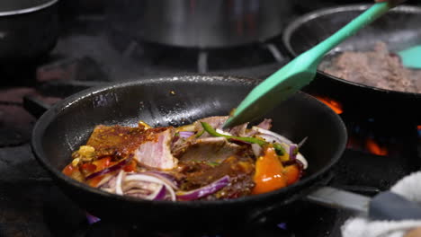 el chef profesional de un restaurante gira con gracia las verduras salteadas en una sartén chisporroteante sobre una llama de fuego alto en la estufa, las chispas vuelan mientras el cocinero sacude la sartén sobre el quemador de gas de la cocina, cámara lenta de primer plano 4k