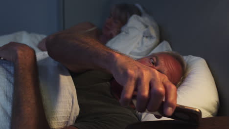 sleepless senior man in bed at night using mobile phone