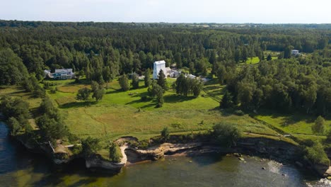 aerial drone footage flying above and in front of a white colored historic wooden lighthouse in muraste on a sandstone cliff bank beach shoreline or seaside during a summer sunny day. rocky beach