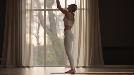 a young woman in white sportswear is stretching with a large hall with large windows in a slow-motion scheme the sun's rays shine through the window. healthy lifestyle healthy morning