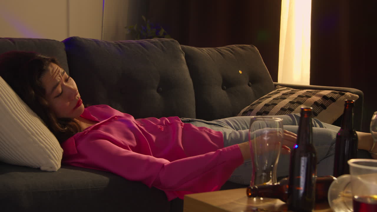 mujer despertando en el sofá después de beber alcohol en la fiesta de la casa sufriendo de resaca respondiendo al teléfono móvil