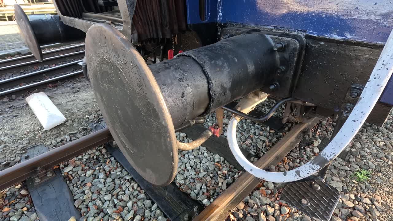 A semi-static shot of a coupler on a passenger carrier on a steam engine locomotive. It's stationed in a railway yard.