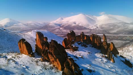 Rocks-in-winter-shot-from-a-drone-in-sunny-weather-against-the-backdrop-of-mountains-and-blue-sky-4k