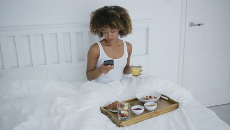 mujer con teléfono disfrutando del desayuno en la cama