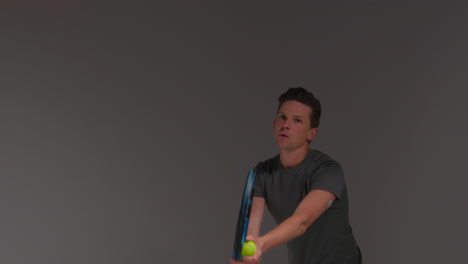 studio shot of male tennis player serving in match hitting ball with racket against grey background 1