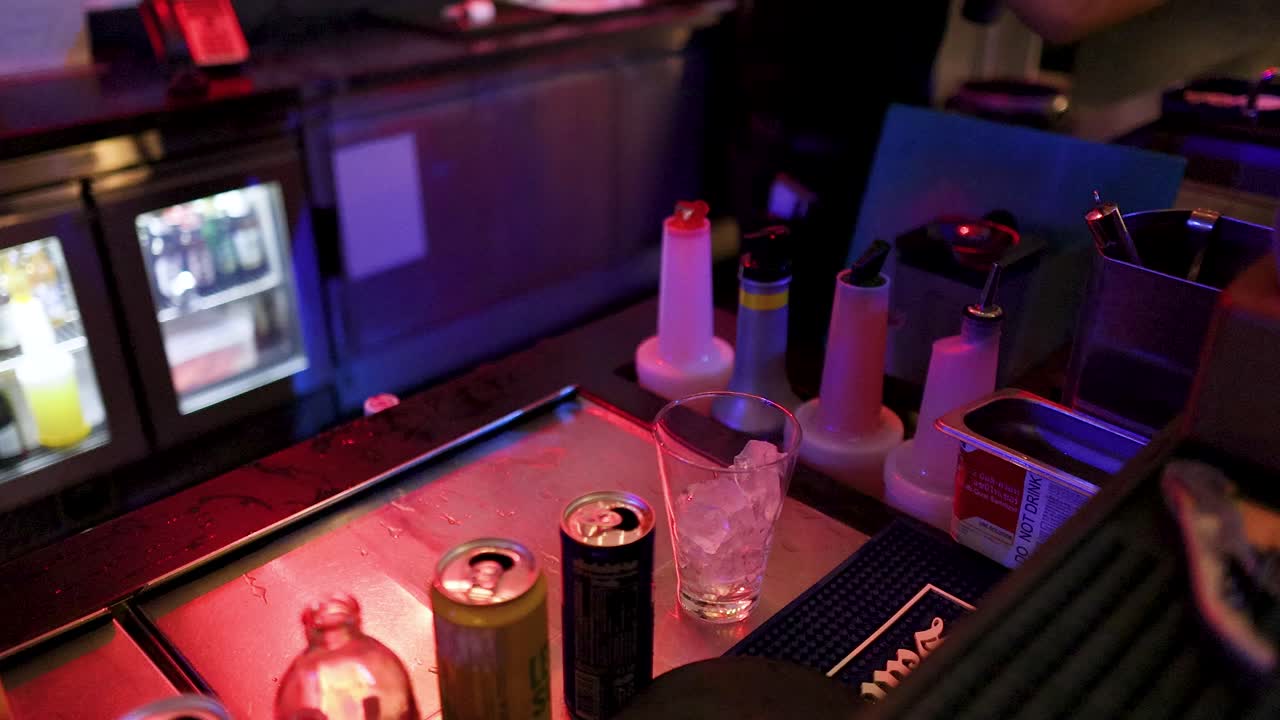 Bartender prepares cocktail with shaker at nightclub bar, colorful lighting, close-up, dynamic movement