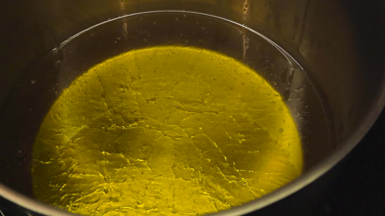 Riprese ravvicinate di olio giallo dorato per frittura profonda, caldo e che inizia a bollire e schiumare a causa dell'alta temperatura. L'olio è in una pentola di acciaio grigio metallizzato su un fornello, con texture.