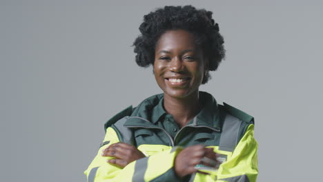 studio portrait of smiling young female paramedic in uniform against plain background