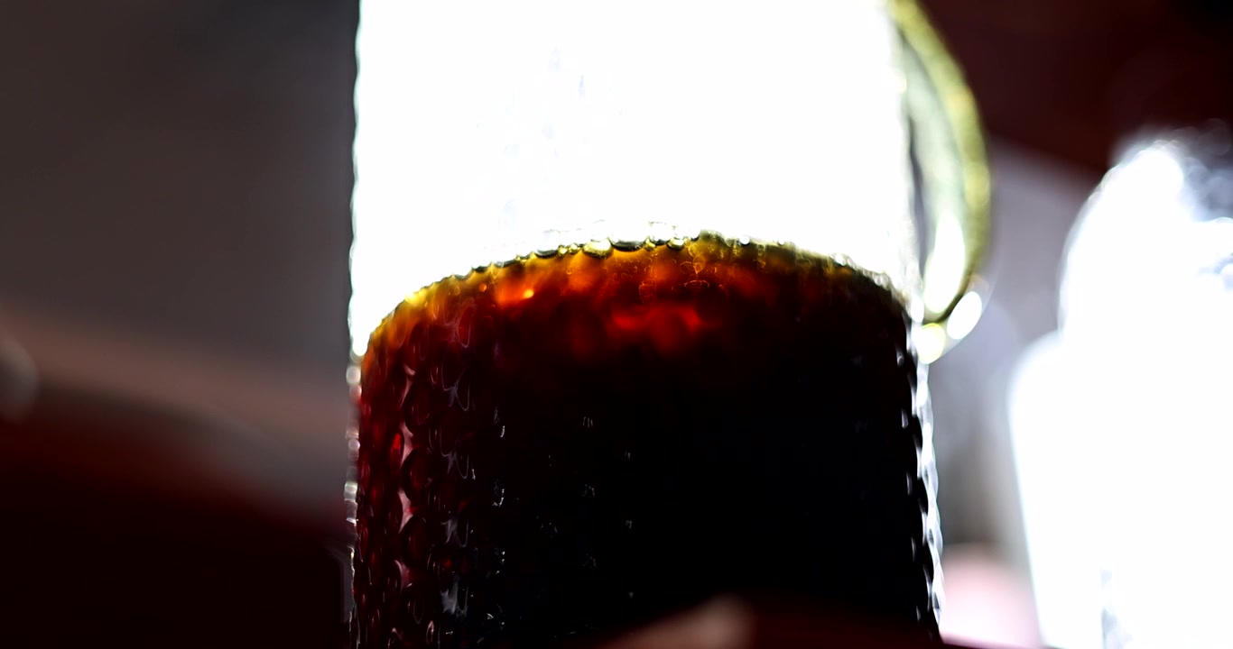 Dettagli macro di caffè scuro appena fatto all'interno di una caraffa di vetro testurizzata con forte controluce, angolazione verso l'alto, liquido nero che schizza