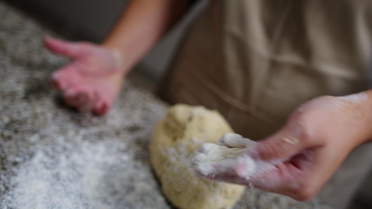 Close-up of a woman's hand spreading flour near dough on a countertop.