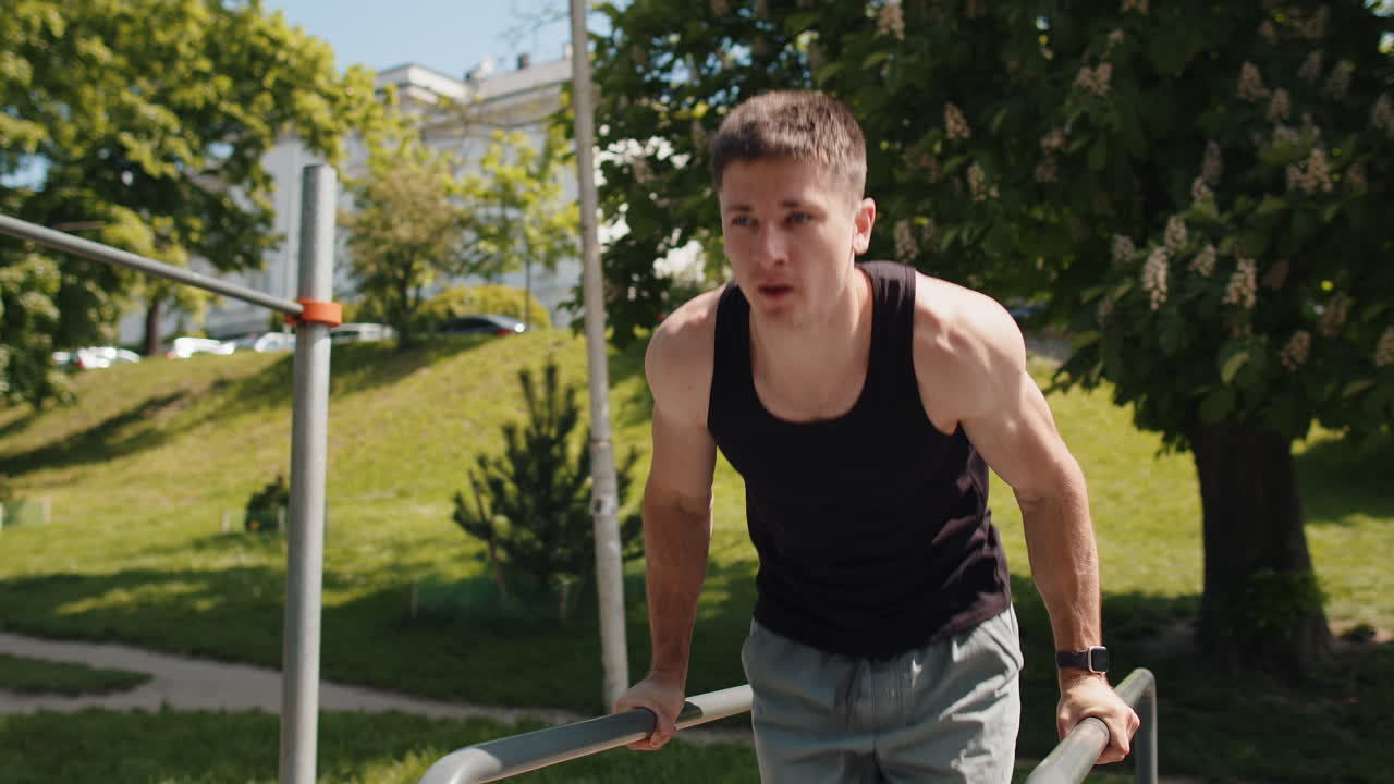 Athletic caucasian man in sportswear practicing dips on parallel bars training triceps on playground