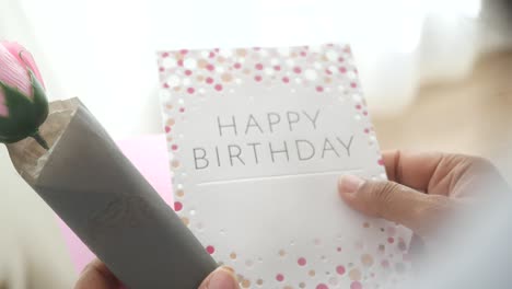 person holding a birthday card and a pink rose
