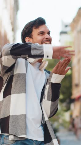 cheerful rich indian man showing wasting throwing money around hand gesture standing on city street