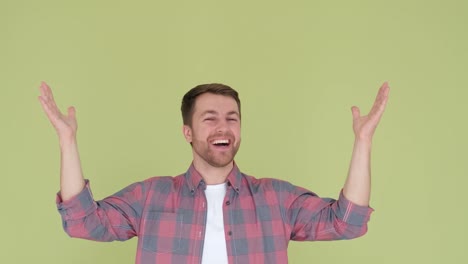 portrait of a happy man in simple clothes smiling and raising his hands up to the camera portrait of a happy man in simple clothes smiling and raising his hands up to the camera isolated on green background
