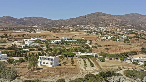 paros greece aerial v6 drone reverse flying shot overlooking scattered coastal homes, panning reveals secluded paralia lolantonis beach with beautiful mountainscape background - september 2021