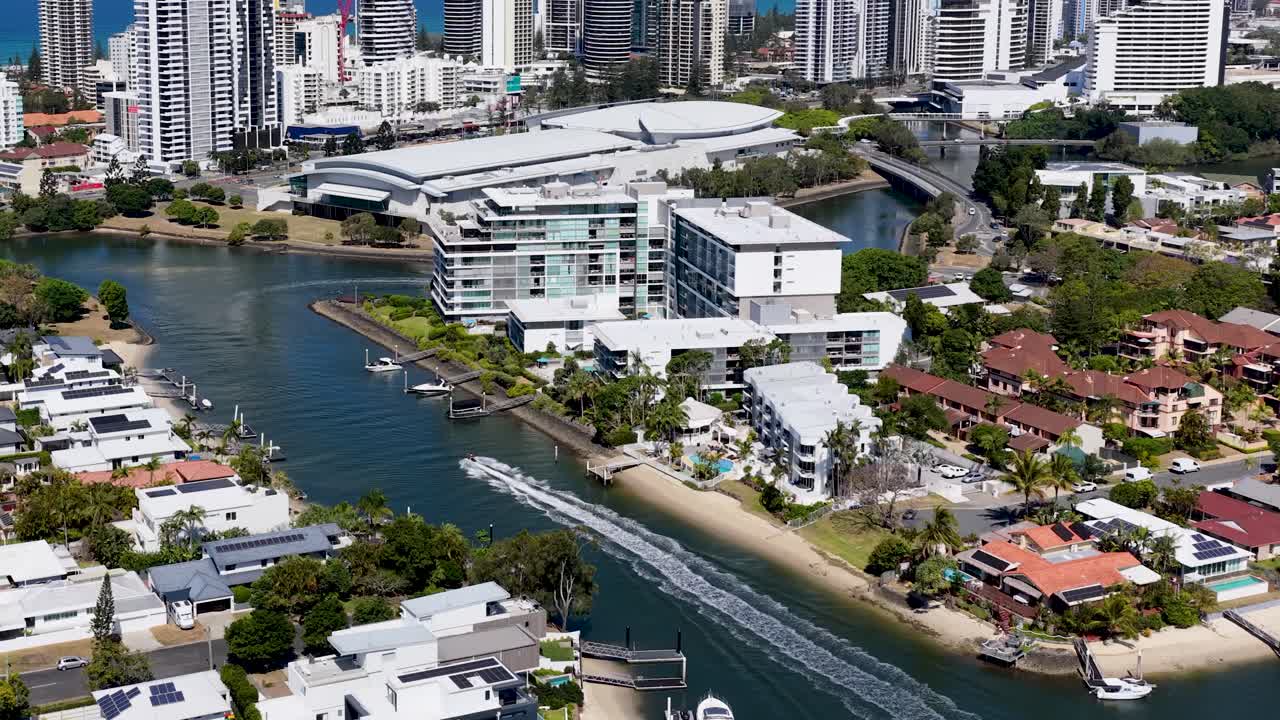 Drone glides above river, waterfront homes, and high-rise buildings under bright midday sunlight