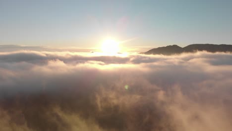 aerial descent into foggy valley sunrise, sun over misty sea of cloud