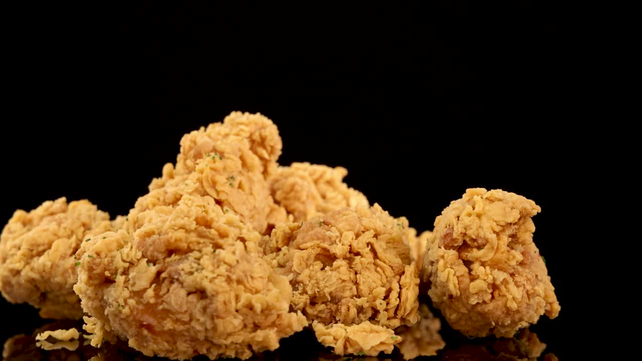 Golden, crumbed chicken breasts and thighs rotate and zoom in slow motion against a black background, highlighting crunchy texture and appetizing detail