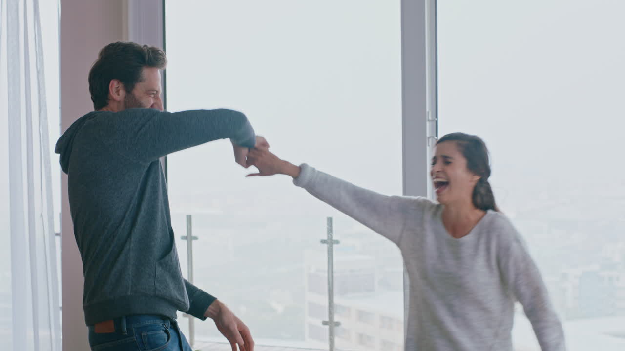 행복한 젊은 커플이 집에서 춤을 추고 성공적인 휴가를 즐기고 즐겁게 휴일에 라이프 스타일을 축하하고 거실에서 유쾌한 춤을 추고 있습니다.