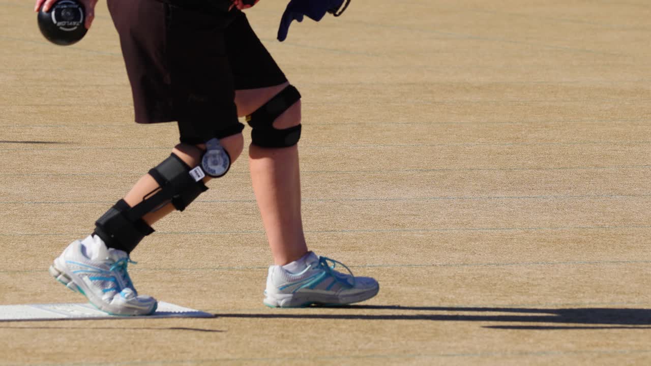 A person with knee braces rolls a lawn bowl on a sunny day at Broadbeach, Gold Coast, showcasing precision and focus