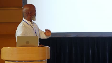 senior african american businessman speaking on stage at podium in auditorium 4k