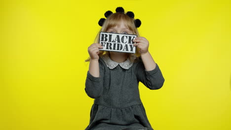 child girl showing black friday inscription, smiling, looking satisfied with low prices, discounts