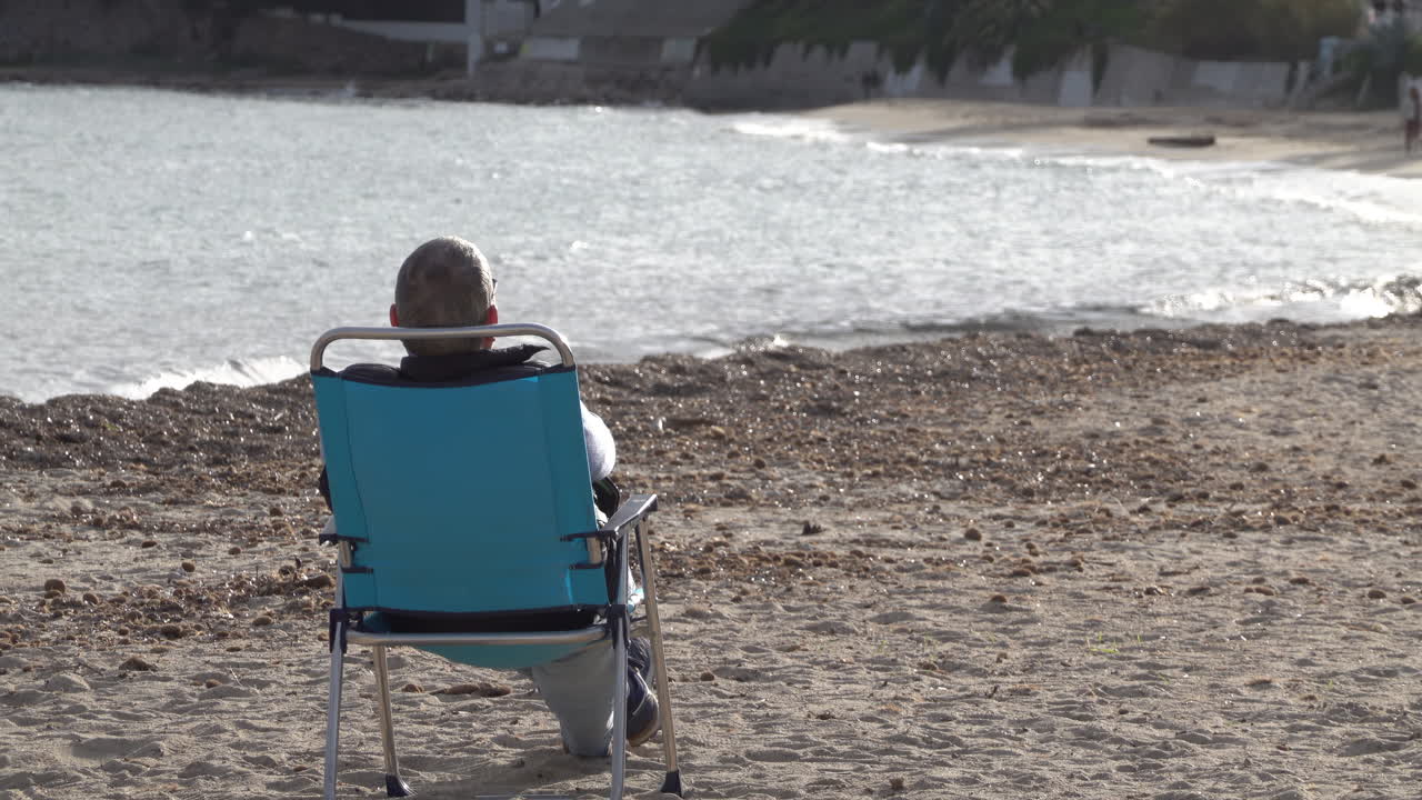 Man resting on a chair, looking at the sea, on the beach