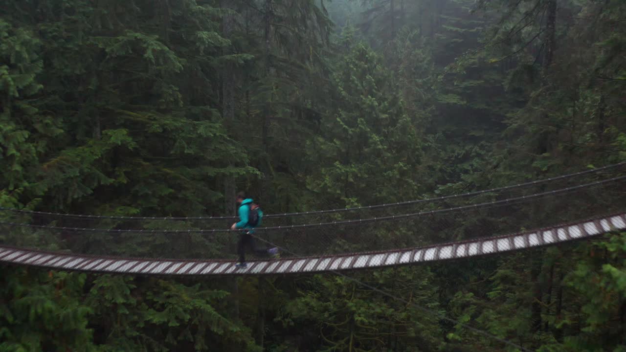 울창 한 숲 에 있는 서스펜션 브릿지 에서 달리는 사람 의 공중 촬영
