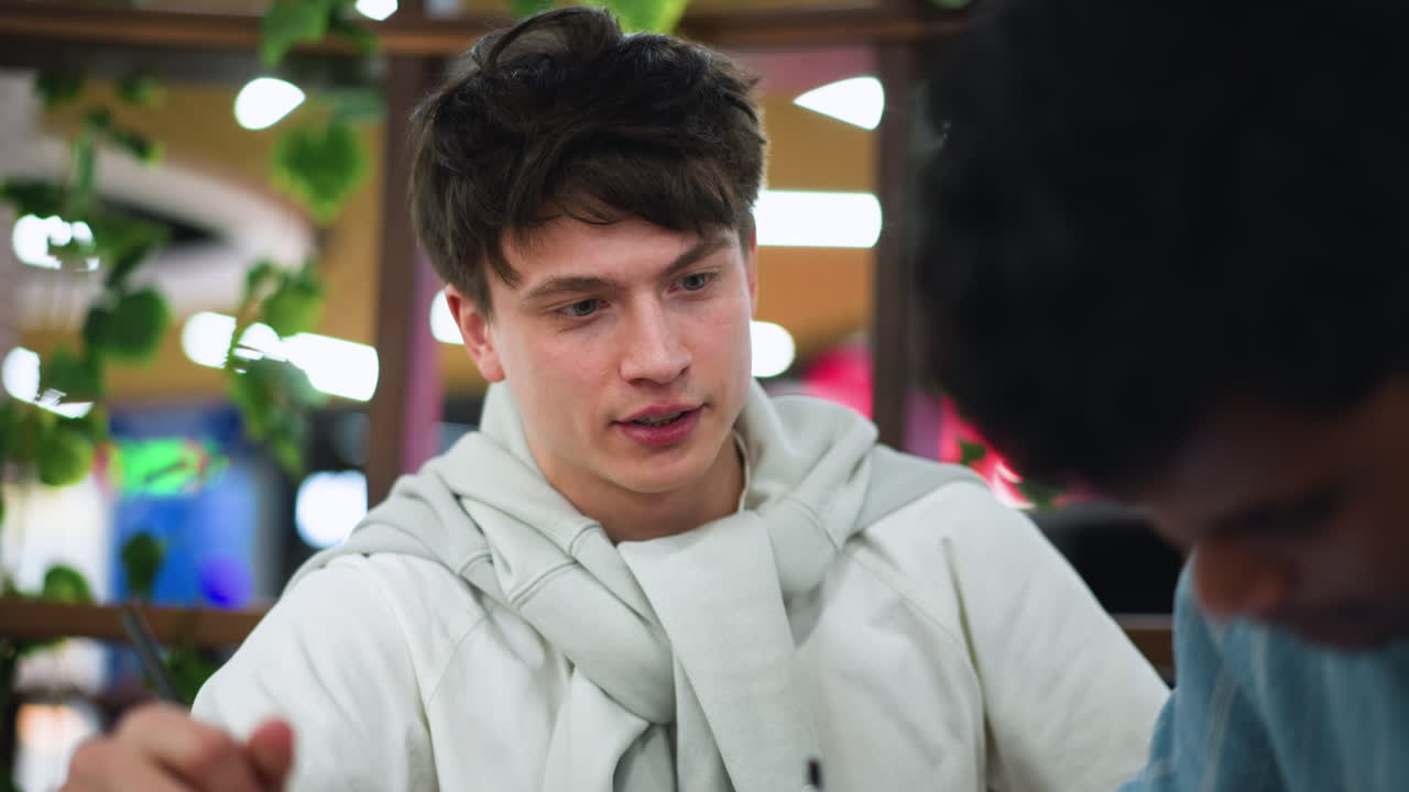 Young lad intently watching colleague draw detailed sketch on paper at wooden desk immersive focus moment capturing creative collaboration inspiration interaction during art session close view scene