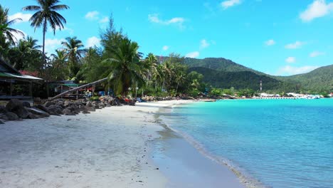 Paradise-beach-with-white-sand-washed-by-calm-clear-water-of-turquoise-lagoon-and-palm-trees-on-shore-of-tropical-island-in-Thailand