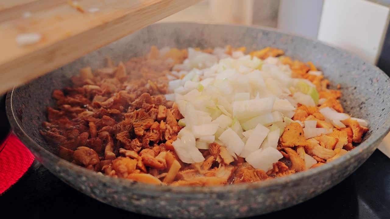 Slow motion macro shot of onions mixing with golden chanterelles in hot pan