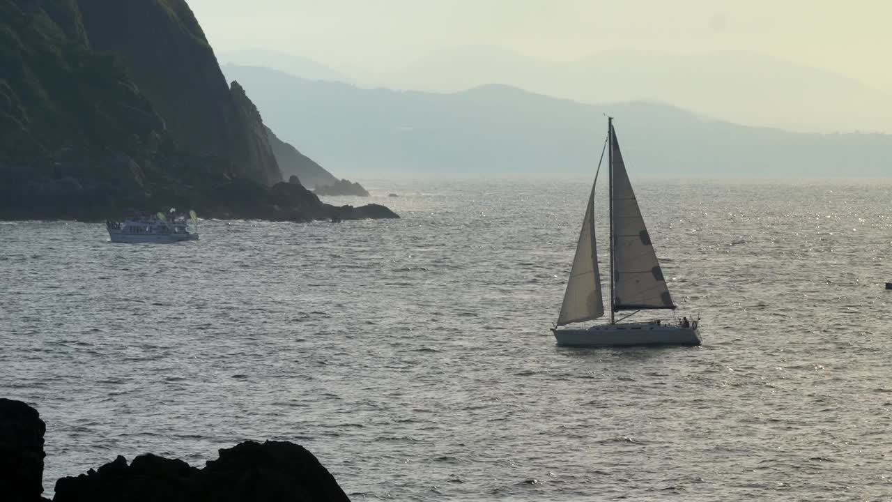 velero que regresa al puerto en una tarde soleada con luz dorada que atraviesa, san sebastián españa, tiro estático