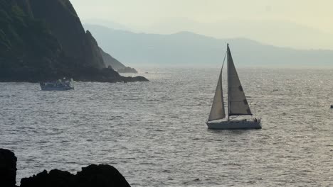 sailboat returning to the harbor on a sunny afternoon with golden light coming through, san sebastian spain, static shot