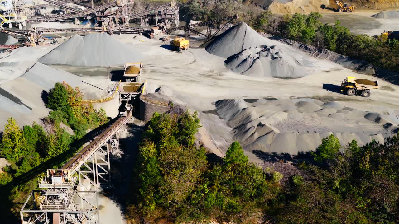 Active quarry with dump trucks transporting fill and aggregate mounds, aerial slow motion overview