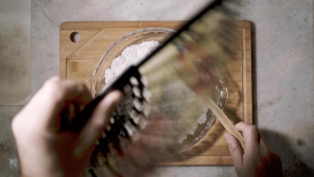 vista de arriba hacia abajo en el mostrador de la cocina con un tazón de vidrio de arroz de sushi y una mano dividiendo semillas de chai en el plato como parte de una receta