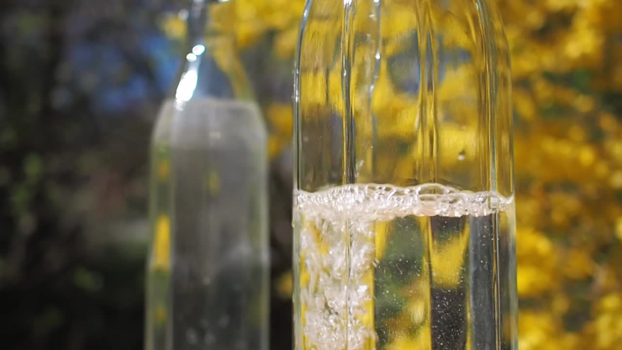 Versare acqua in una bottiglia di vetro su sfondo giallo e floreale.
