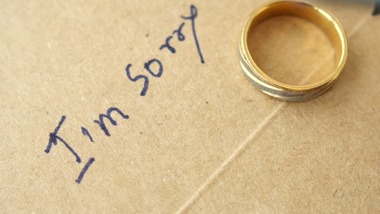 Someone writing 'sorry' on a card with a ring nearby