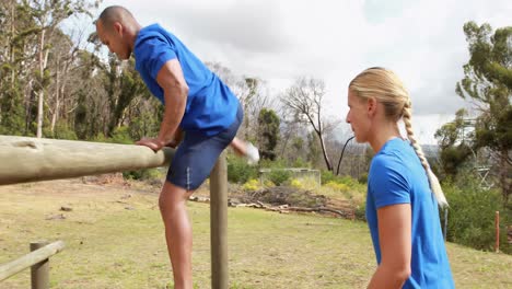 entrenador masculino ayudando a una mujer a escalar un obstáculo durante una carrera de obstáculos