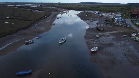 aerial drone shot flying over creek at low tide with sailing boats in north norfolk on cloudy gloomy moody day uk