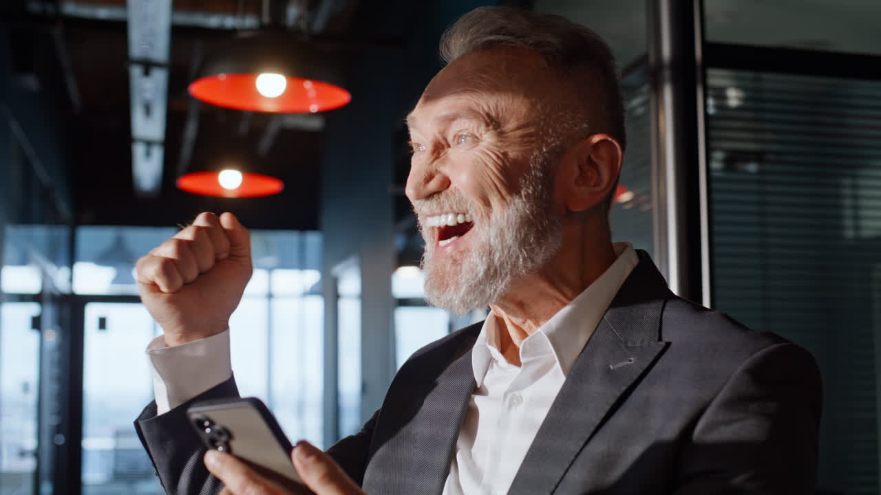 Pensionato entusiasta che guarda da vicino il cellulare in un corridoio. Uomo anziano sorridente