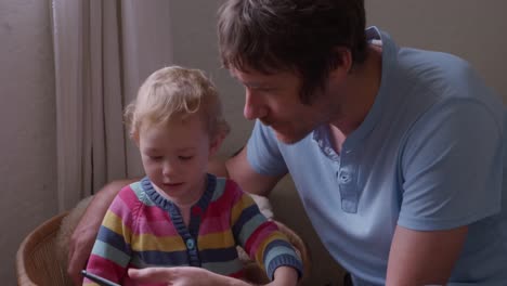 Caucasian-man-with-baby-looking-smartphone-at-home