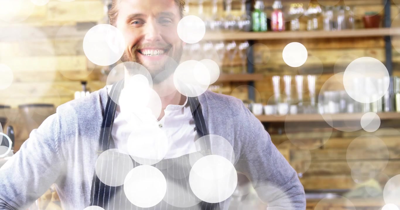 Con la telecamera che si muove verso l'alto, un barista sorridente al bancone del caffè accoglie i clienti con un effetto bokeh.