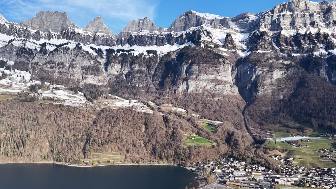 Vista aerea rotante di un drone su Walenstadt, in Svizzera. Ripresa dell'ampia valle invernale e dell'imponente catena montuosa Churfirsten, ricoperta di neve, sotto un cielo terso