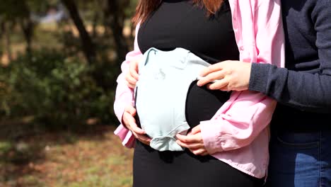 male touching the belly of a pregnant woman shows a baby bodysuit