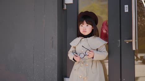 korean girl in a gray coat and cap stands the street in spring at the glass doors of the store