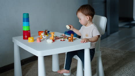 caucasian child playing with toy animals and game with fruit. little baby plays at desk.