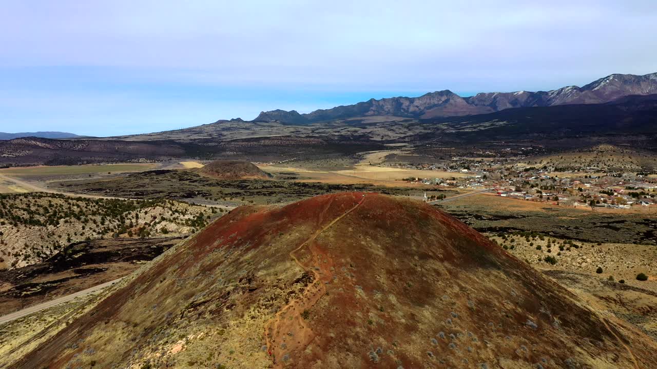 View of tourists descending a natural footpath from a high hill overgrown with bushes in a mountainous valley on a sunny day