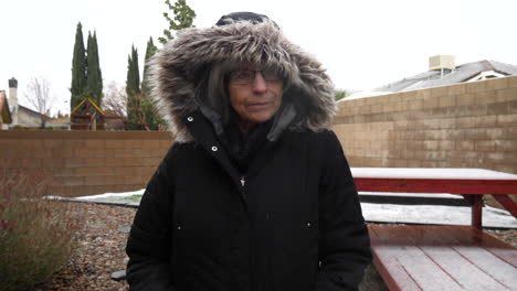 una mujer con un cálido abrigo de invierno caminando mientras los copos de nieve y el granizo caen en una helada tormenta de invierno a cámara lenta