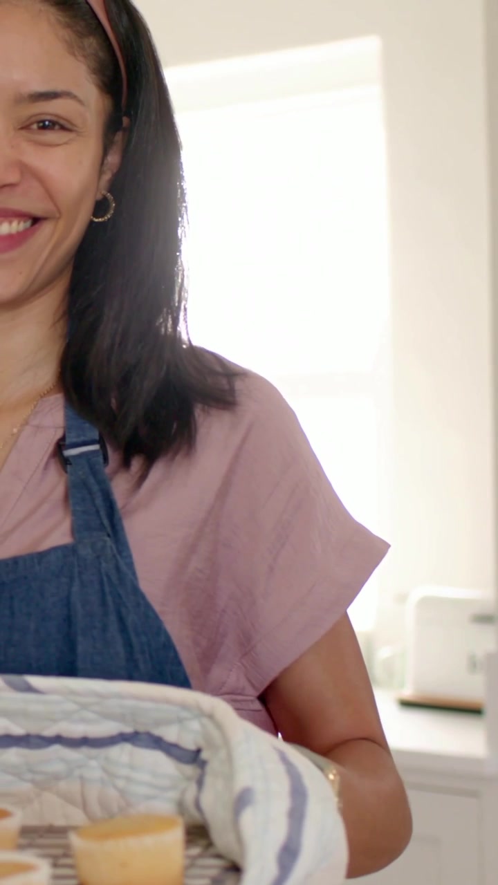 Video verticale: Panettiere che cammina con grembiule e maglietta rosa, si gira mostrando muffin su una griglia in cucina, con spazio per il testo