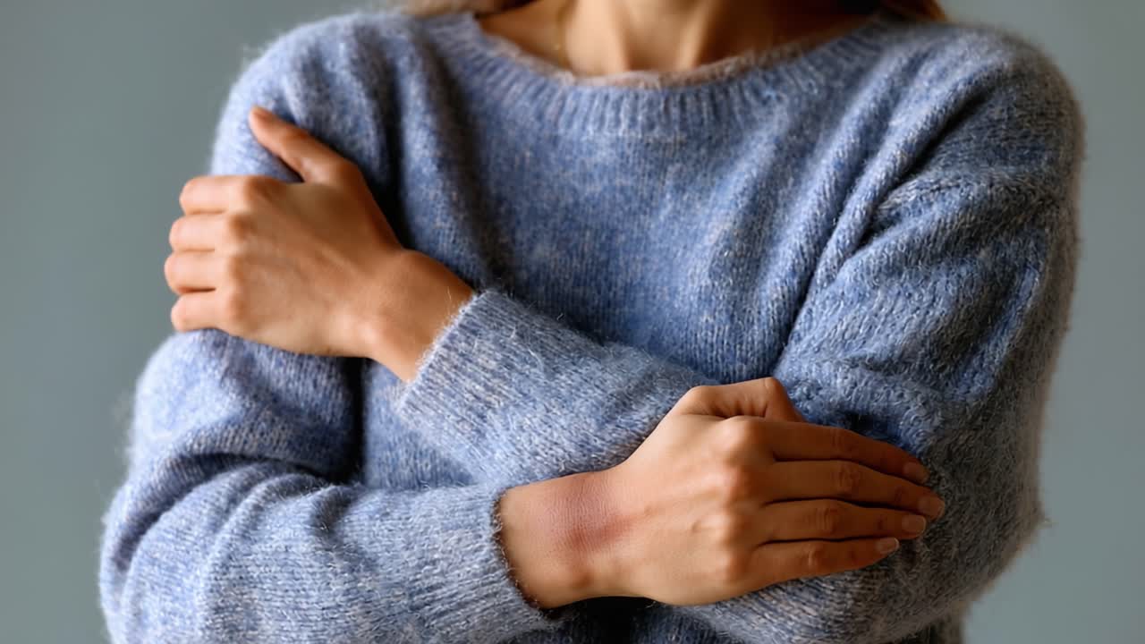 Uma modelo exibe um suéter aconchegante e macio em um ambiente interno sereno, transmitindo calor e conforto através do abraço suave de seus braços que destacam a textura da peça.